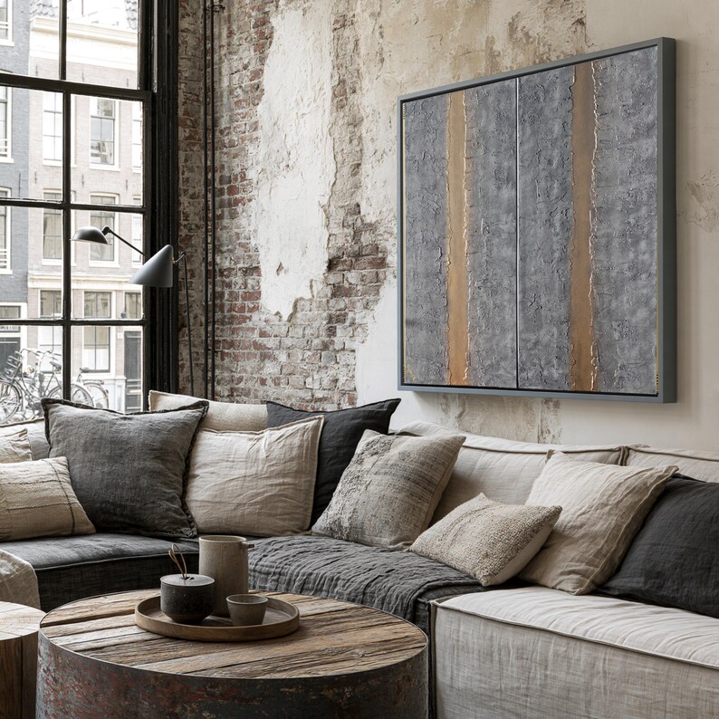 a cozy living room with a large window overlooking a cityscape. The room features a comfortable couch with a wooden coffee table in front of it, and a large abstract painting on the wall. The overall decor has a rustic and modern aesthetic, with a mix of neutral colors and natural textures.