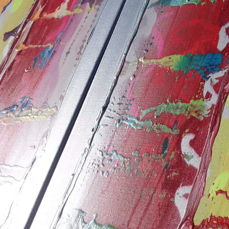 The image is a close-up of a vibrant, abstract painting with bold colors and brushstrokes. The painting appears to be a mix of red, green, and yellow hues, with some areas of white and blue. The brushstrokes are visible, adding texture and depth to the artwork.