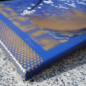 The image is a close-up of a blue and gold canvas with a floral design, featuring a golden flower and a blue background.