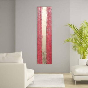 a modern living room with a tall, vertical red and white abstract painting hanging on the wall. The room is furnished with two white sofas and a large potted plant, creating a clean and minimalist aesthetic.