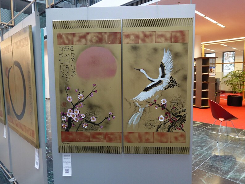 a large, colorful painting of a crane in flight, with a background of flowers and a sun. The painting is displayed on a wall, and there is a red chair visible in the background.
