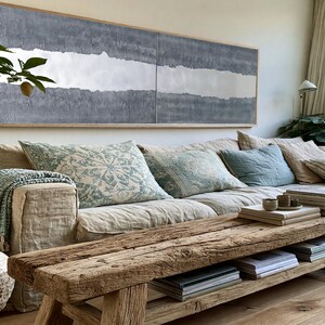 a cozy living room with a large window, a comfortable sofa with patterned pillows, a wooden coffee table, and various decorative elements such as a potted plant, a vase, and a painting on the wall.