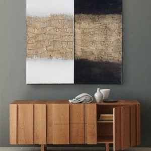 Peut inclure: Tableau abstrait divis&eacute; en deux parties : blanc et noir. Chacune pr&eacute;sente une bande horizontale textur&eacute;e dor&eacute;e. En dessous, un meuble en bois moderne avec une porte partiellement ouverte.