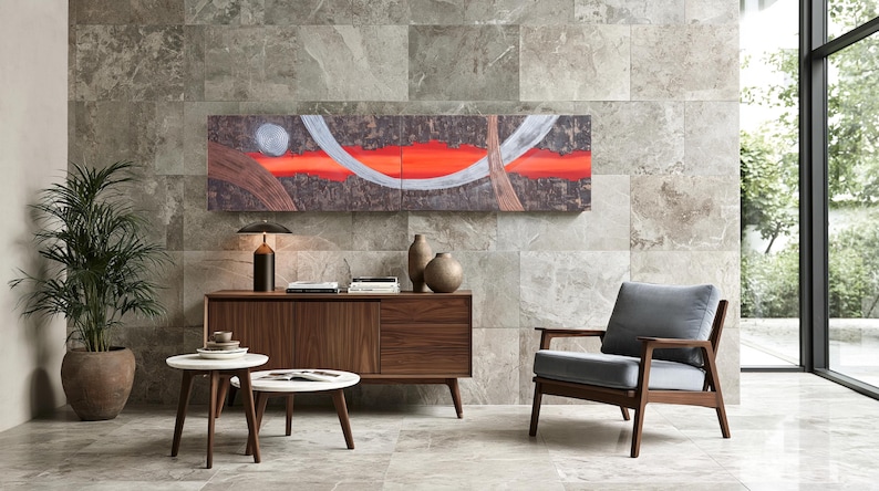 a modern living room with a large abstract painting on the wall, a wooden sideboard with a lamp and decorative items, a gray armchair, and a round coffee table.