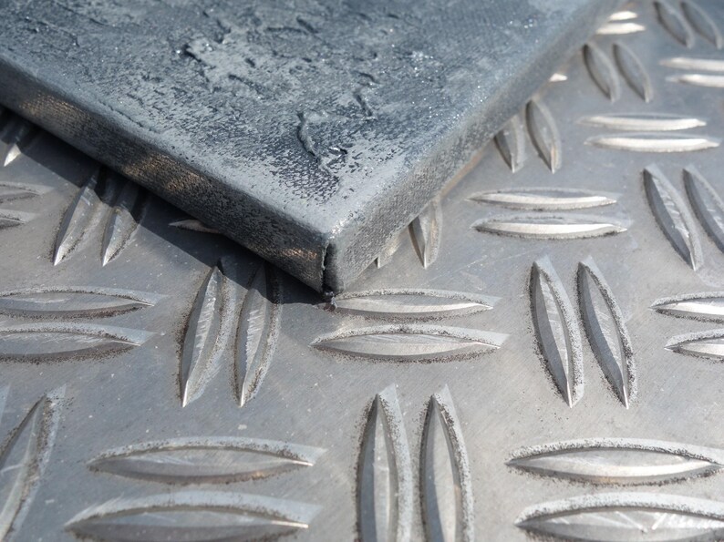 a close-up view of a metal surface with a diamond-patterned texture, featuring a dark gray or black metal piece with a rough, textured surface.