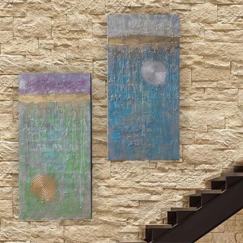 two abstract paintings hanging on a brick wall, with a staircase visible in the background.