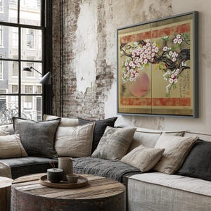 a cozy living room with a large window overlooking a cityscape. The room is furnished with a gray sofa, a wooden coffee table, and a large framed artwork featuring a floral design. The artwork is mounted on the wall above the sofa, creating a visually appealing focal point in the space.