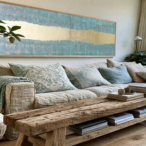 a cozy living room with a large window, a comfortable sofa with patterned pillows, a wooden coffee table, and a large abstract painting on the wall.