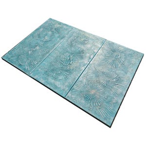 a blue tile with a repeating pattern of white and green designs, including a floral pattern and a fan-like design.