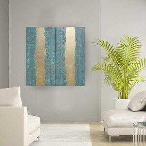 a modern living room with a large abstract painting featuring blue and gold vertical stripes hanging on the wall. The room is furnished with two white sofas and a large potted plant, creating a serene and stylish atmosphere.