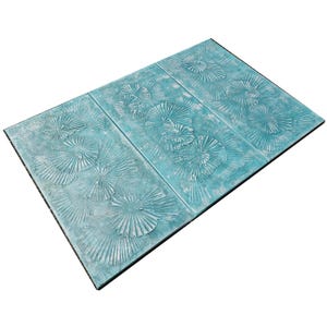 a decorative tile with a repeating pattern of white and blue designs, including a floral motif and a fan-like pattern.