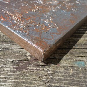 a close-up view of a metal surface with a textured, rusty appearance, resting on a wooden surface with visible cracks and peeling paint.
