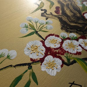a close-up view of a painting depicting a branch with white flowers and green leaves.