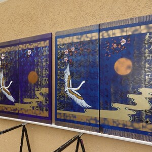 two large paintings displayed on a wall, each depicting a crane in flight against a night sky background.