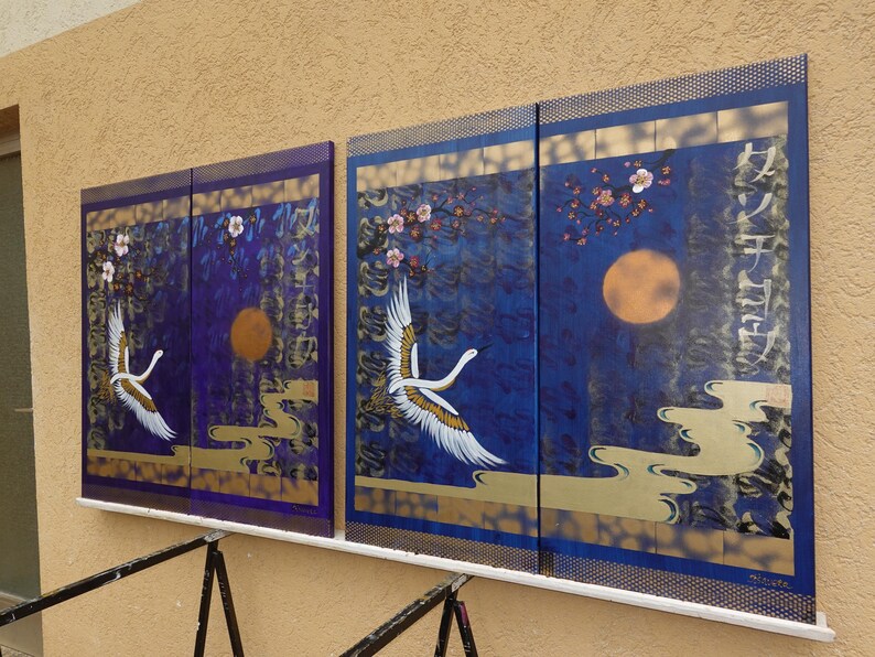 two large paintings displayed on a wall, each depicting a crane in flight against a night sky background.