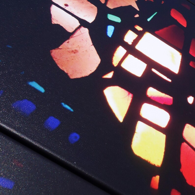 The image is a close-up of a colorful stained glass window, with various shades of red, orange, yellow, and blue creating a vibrant and intricate pattern.