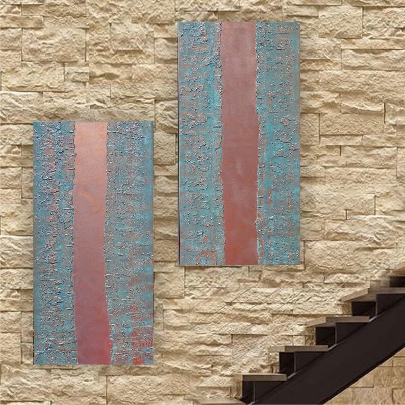 two abstract paintings hanging on a brick wall, with a staircase visible in the background.