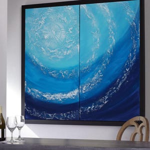 a large, vibrant painting of a blue ocean scene, with swirling patterns and textures that create a sense of movement and depth. The painting is framed and hangs on a wall, with a wooden chair visible in the foreground.