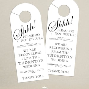 Może przedstawiać: Dwa białe wieszaki na drzwi z tekstem "Shhh! Proszę nie przeszkadzać. Odzyskujemy siły po ślubie Thorntonów. Dziękujemy!" w czarnym, ozdobnym pismie.