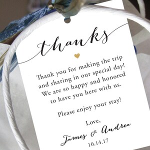May include: White thank you tag with black calligraphy that reads "thanks". The tag has a gold heart and text that reads "Thank you for making the trip and sharing in our special day! We are so happy and honored to have you here with us. Please enjoy your stay! Love, James & Andrea 10.14.17"