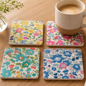 May include: Four square coasters featuring distinct floral patterns with vibrant colors including yellow, pink, and blue. Each coaster displays a dense, intricate botanical print on a light background, showcasing a variety of small flower shapes.