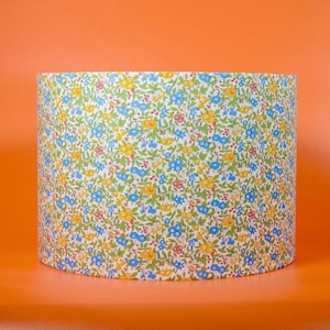 Può includere: Un paralume bianco con un motivo floreale in tonalità blu, giallo e rosso. Il motivo è una stampa floreale a piccola scala su sfondo bianco.