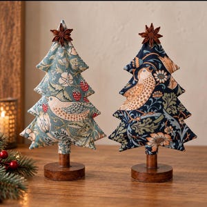 May include: Two fabric Christmas tree ornaments on wooden stands. The left tree features a light blue background with a bird, strawberry, and floral pattern. The right tree has a dark navy background with a bird and floral print. Both are topped with a star anise.