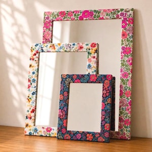 May include: Three rectangular mirrors with flat frames featuring vibrant floral patterns. The largest frame has a pink and green floral print, the medium frame has a multi-colored floral design, and the smallest frame has a dark blue floral pattern.
