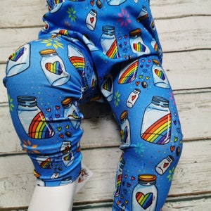 Op de afbeelding: Blauwe leggings met een patroon van regenboogpotten gevuld met harten. De potten hebben een wit deksel en een regenboog erin.