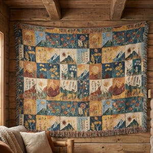 May include: A woven throw blanket with a patchwork design featuring mountain and floral scenes in shades of blue, yellow, and brown. The blanket has a fringed edge and is displayed on a wooden wall.