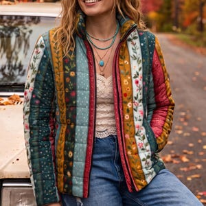 May include: A quilted puffer jacket featuring vertical stripes in shades of teal, mustard yellow, and deep red, adorned with floral and botanical patterns. The jacket has a high collar, a front zipper, and is worn over a cream lace top and blue jeans.