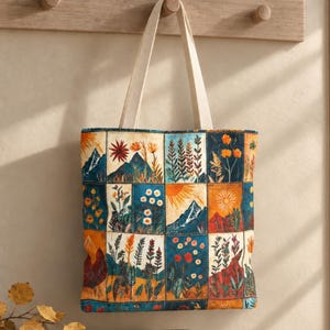 May include: A rectangular tote bag featuring a grid pattern of various illustrations including mountains, suns, and diverse floral arrangements in shades of blue, orange, yellow, and green, equipped with two long, light-coloured fabric shoulder straps.