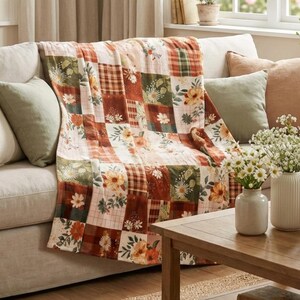 May include: A patchwork throw blanket with floral and plaid patterns in shades of orange, green, and cream. The blanket is draped over a beige sofa with matching throw pillows. The throw blanket is a cozy home decor item.