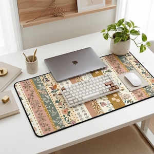 May include: A floral patterned desk mat with a black border. The mat features vertical stripes in various colors, including pink, green, and beige, with floral and leaf designs. A laptop, keyboard, and mouse are on the mat.