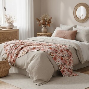 May include: A bed is made with a light beige comforter and pillows. A pink and white patterned throw blanket with strawberries and flowers is draped over the bed. A woven basket and a round mirror are also in the room.