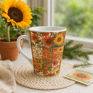 May include: A white-handled mug with a sunflower design. The mug features a patchwork pattern of orange, yellow, and green floral images. A sunflower plant in a terracotta pot is in the background, along with a beige coaster.