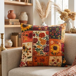 May include: A square throw cushion featuring a patchwork design of various floral patterns. The print includes sunflowers, roses, and assorted wildflowers in warm autumn tones of orange, yellow, deep red, and dark green on a cream background.