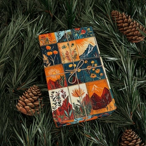 Könnte beinhalten: Ein verpacktes Geschenk mit einem farbenfrohen Patchwork-Design mit Berg- und Blumenillustrationen. Das Geschenk ist mit Bindfaden gebunden und liegt auf einem Bett aus grünen Kiefernnadeln, mit Kiefernzapfen verstreut.