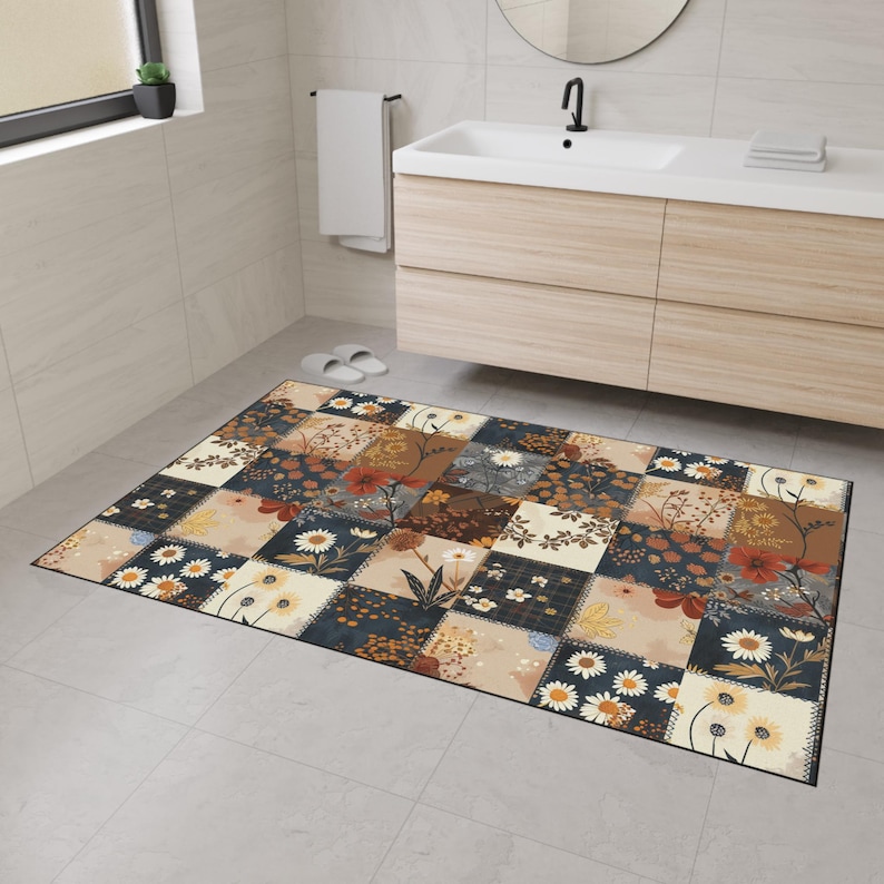May include: A rectangular patchwork bath mat featuring a variety of floral patterns in shades of beige, navy, brown, and cream. The mat is placed on a tiled floor in a bathroom setting, with a sink and mirror visible in the background.