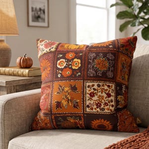 Könnte beinhalten: Ein quadratisches Zierkissen mit einem Patchwork-Design aus verschiedenen herbstlichen Illustrationen wie Sonnenblumen, Kürbissen und Herbstlaub in Orange-, Braun-, Gelb- und Cremetönen, abgerundet durch ein kleines Etikett an der Seite.