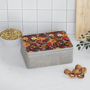 May include: A rectangular gray storage box with a floral pattern on the lid. The lid features a dark background with orange, yellow, and red flowers. The box is sitting on a white surface.