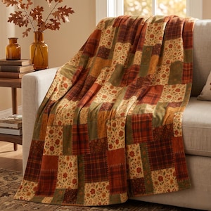 May include: A patchwork throw blanket featuring a repeating pattern of squares in shades of orange, brown, and olive green. The design alternates between floral prints with small red and yellow flowers and dark plaid squares with intersecting lines.
