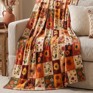 May include: A rectangular throw blanket featuring a patchwork design of various floral patterns. The print consists of squares displaying sunflowers, daisies, and other autumn-toned blossoms in shades of orange, yellow, red, brown, and green.