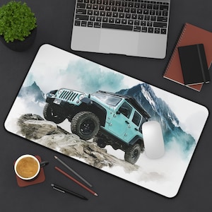 May include: A light blue Jeep mouse mat featuring a watercolour illustration of a Jeep climbing a rocky terrain with a mountain backdrop. The mat has a black border and is surrounded by a laptop, coffee cup, and office supplies.