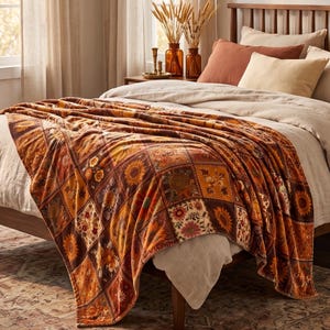 Può includere: Una morbida coperta con un design patchwork caratterizzato da vari motivi floreali e di girasoli nei toni dell'arancione, marrone, giallo e crema. La coperta è drappeggiata su un letto con biancheria dai colori neutri, inclusi cuscini e copripiumino.