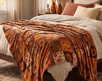 May include: A soft throw blanket featuring a patchwork design of various floral and sunflower patterns in shades of orange, brown, yellow, and cream. The blanket is draped over a bed with neutral-coloured bedding, including pillows and a duvet cover.
