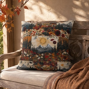 May include: A square throw cushion featuring a woven tapestry design of a mountain landscape under a bright sun, surrounded by a dense field of colourful red, orange, and yellow wildflowers and dark green pine trees in a repeating pattern.