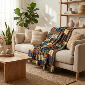 Puede incluir: Un sof&aacute; beige con cojines y una manta de retazos. La manta presenta un dise&ntilde;o floral y paisaj&iacute;stico en tonos azules, naranjas y amarillos. Una mesa de centro de madera y una alfombra de yute completan la escena. Ambiente c&aacute;lido.