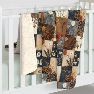 May include: A patchwork blanket with a floral design in shades of brown, navy, and cream. The blanket is draped over a white crib rail, showcasing the soft, sherpa-lined backing.