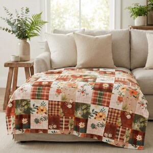 May include: A patchwork throw blanket with a mix of floral, plaid, and solid squares in shades of orange, brown, green, and cream. The blanket is draped over a beige sofa with matching pillows, creating a cozy, inviting atmosphere.